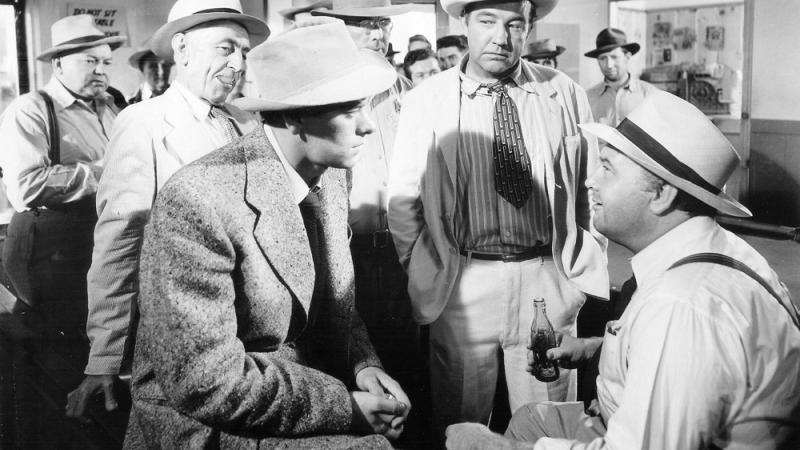 black and white film still of two men talking, a third man watches the conversation