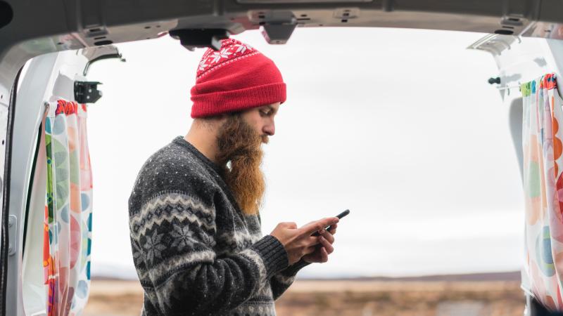 Hipster man looks at his phone in the outdoors. 