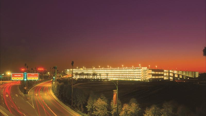 Photograph of a parking structure in distance, highway in foreground, at sunset