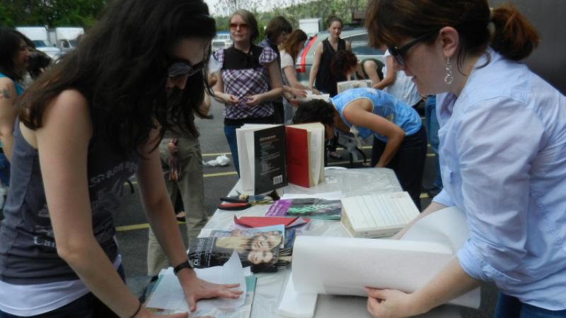 A woman standing behind a table showing another woman how to save a wet book