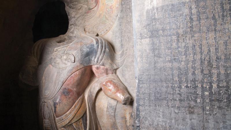 Colored sculpture of a guardian / warrior at the entrance to a cave, with a wall engraving to his right.