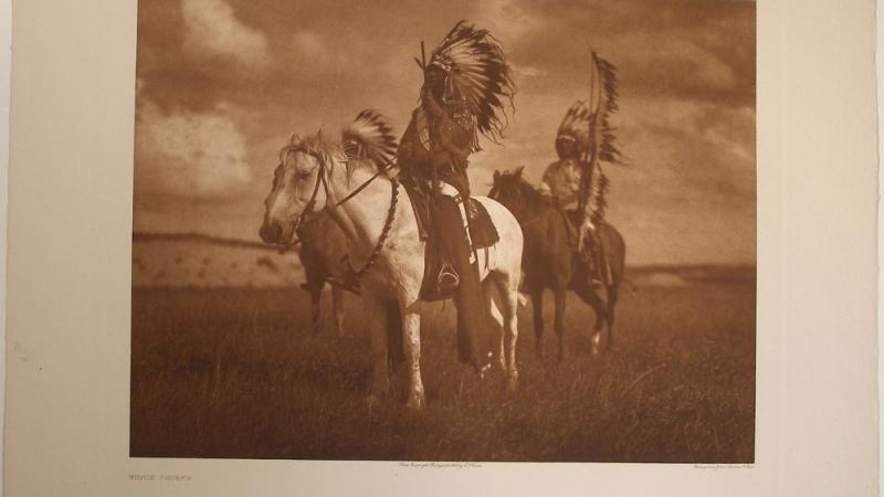 Photograph of a Native American man in a headdress on a horse