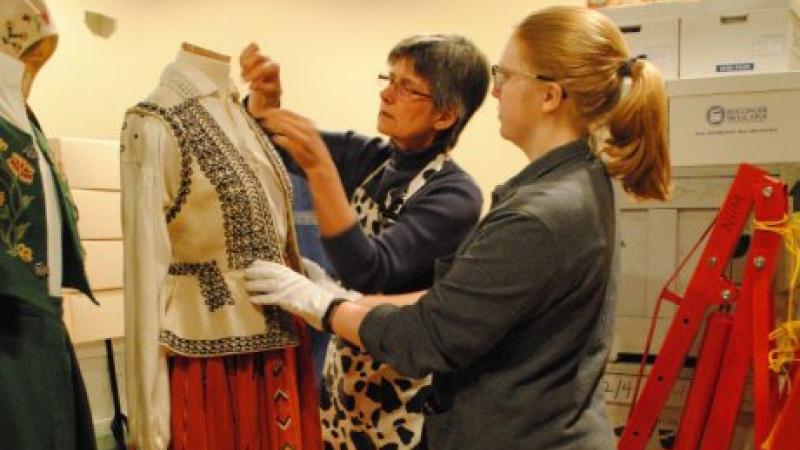 two women examine a costume on a mannequin