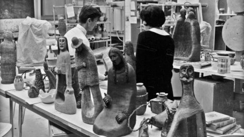 black and white photo of two people in studio, surrounded by ceramic sculptures