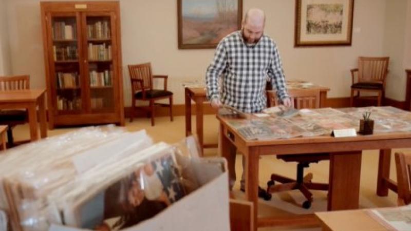 photograph of man looking at sheet of photos in a library