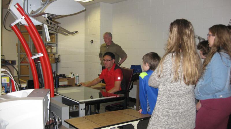 kids stand around viewing an overhead scanner in use