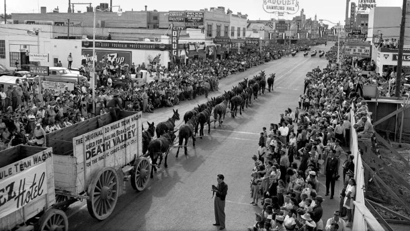 black and white photograph looking down a crowded street, parade occurring