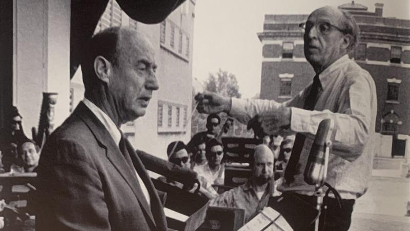 Black and white photo of Copland conducting Lincoln Portrait with Adlai Stevenson at Lewisohn Stadium. 