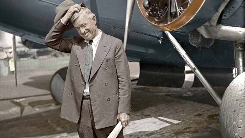 Will Rogers stands in front of a plane