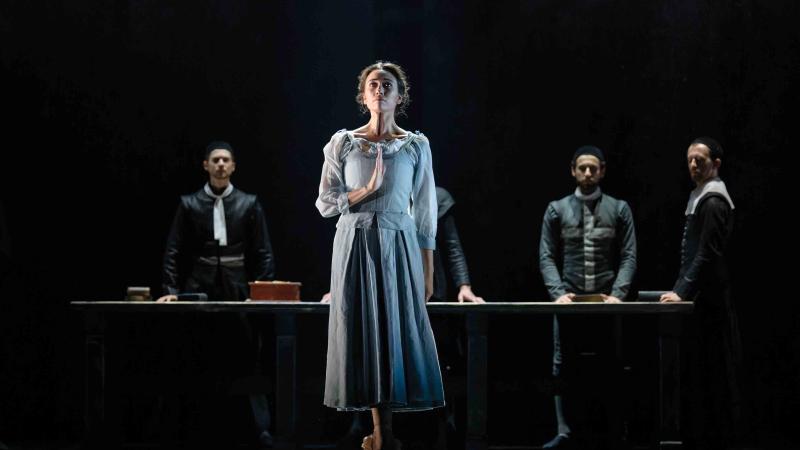 Ballet still from The Crucible, woman standing en pointe in front of 4 men.