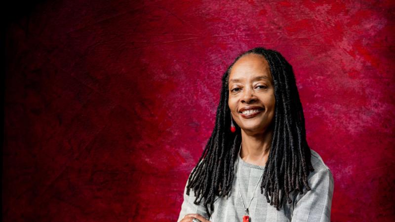 Portrait of Valerie Boyd standing against red background with arms crossed