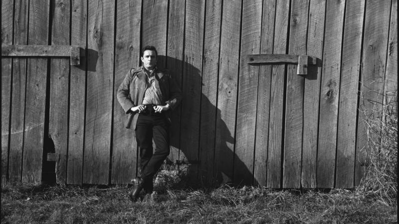 Johnny Cash standing in front of wooden building.