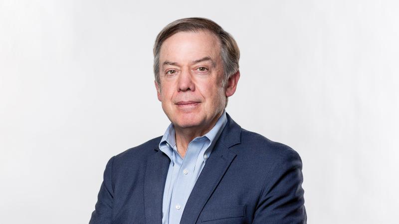 Photograph of Michael Crow, president of ASU, in a navy blue suit and light blue shirt