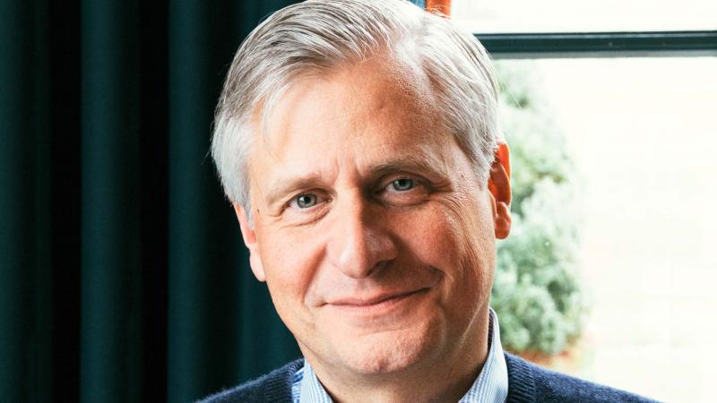 Jon Meacham, silver-haired, standing by a window